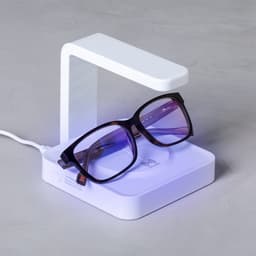 A wireless charger in white, featuring a sleek design, with a pair of purple-tinted glasses resting on it.