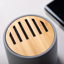 A Bluetooth speaker featuring a grey body and a wooden top with ventilation slots, alongside a smartphone.