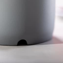 A grey Bluetooth speaker with a textured surface, featuring a small opening at the base. It has a minimalist design.