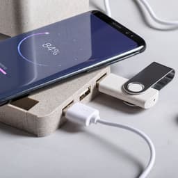 A charging station with a smartphone displaying 84% battery, connected to a USB drive and a white charging cable.