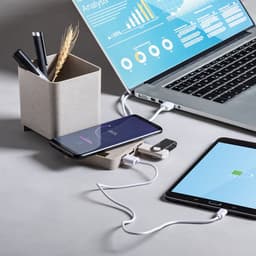 A desk scene featuring a laptop, tablet, smartphone, and a pen holder with pens and decorative elements, all in neutral tones.