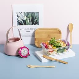 A pink lunch box beside a wooden cutting board, bamboo utensils, a drink bottle, and a dragon fruit on a pastel background.