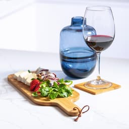 A wooden chopping board with cheese, greens, strawberries, and a blue drink bottle and wine glass beside it.