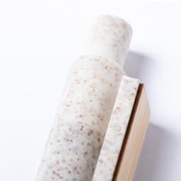 A wooden pen with a speckled white and beige design, resting next to a wooden block, features a logo.