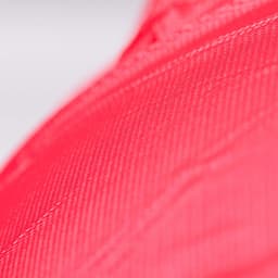A close-up view of textured fabric in bright red colour, featuring a subtle sheen. The item has a logo.