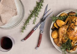 A Bordeaux carving set with stainless steel blades and wooden handles, displayed alongside roasted chicken and herbs.