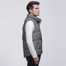 A man models a grey puffer vest with a high collar, worn over a long-sleeve white shirt. The vest has a logo.