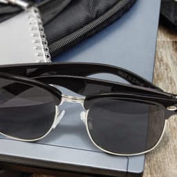 Maverick Sunglasses with a sleek black frame and dark lenses, placed on a surface with a notebook and backpack.