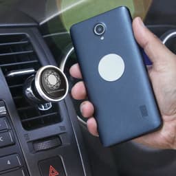 A dark blue smartphone held next to a silver magnetic phone holder attached to a car dashboard.