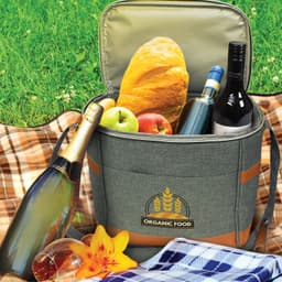 A grey cooler bag with brown accents contains a bottle of champagne, wine, apples, and a loaf of bread.