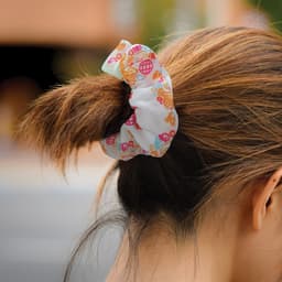 A set of two hair scrunchies in pastel colours with playful patterns, featuring a light fabric texture.