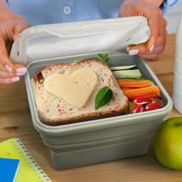 A collapsible lunch box in grey contains a sandwich with heart-shaped cheese, cherry tomatoes, and sliced vegetables.
