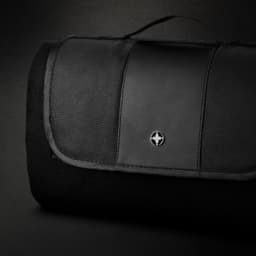 A black picnic blanket with a textured surface and a logo on the top, featuring a foldable design and carrying handle.