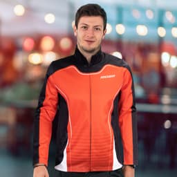 A man in a red and black sports jacket with a logo, smiling against a softly blurred background.