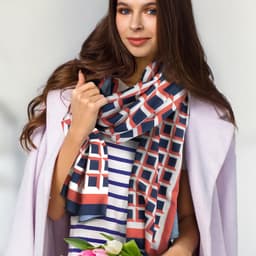 A woman wearing a patterned Berlin scarf in coral, navy, and cream, holding a bouquet of flowers.