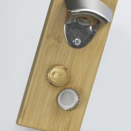 A drink bottle opener made of bamboo featuring a metallic bottle cap opener and two bottle caps.