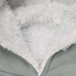 A detail of a soft, fluffy inner lining in a hoodie, featuring grey outer material and textured white fleece.