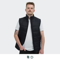A man wearing a black puffer vest over a white t-shirt, standing against a plain background. The vest features a logo.
