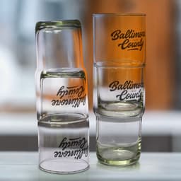 Stackable glass tumblers in clear and frosted finishes, featuring a logo on the side of each glass.