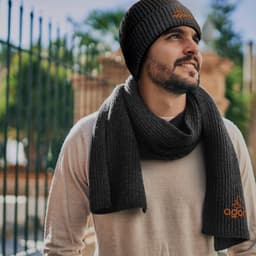 A man wearing a dark grey beanie and matching ribbed scarf, with a logo visible on the scarf.