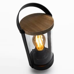 A lantern with a black metal frame, transparent glass, and a wooden top showcasing a glowing light bulb inside.